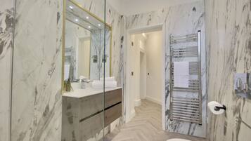 A modern bathroom with marble walls, a glass shower enclosure, a wooden vanity, and a towel rack.