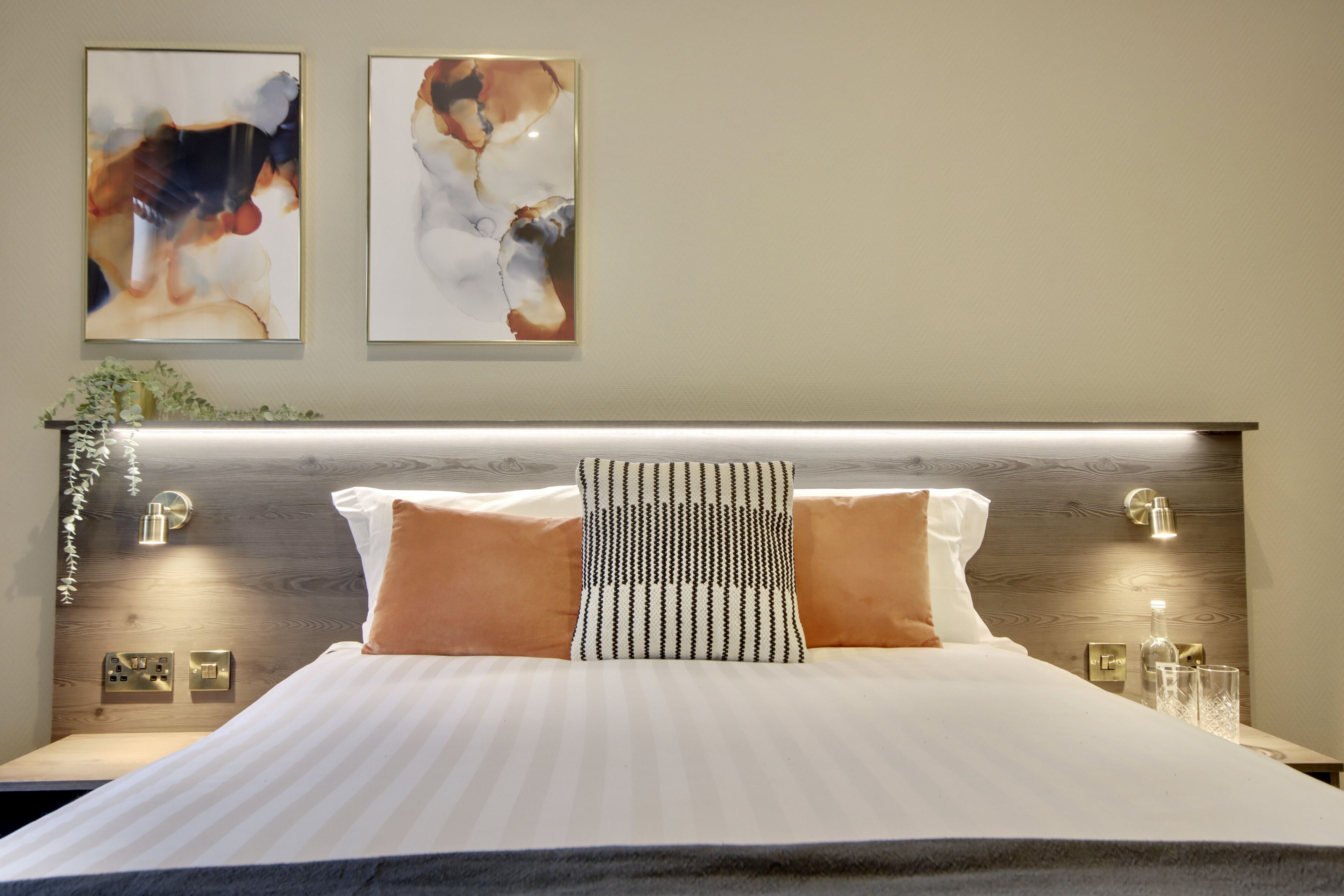 Una cama bien hecha con ropa de cama a rayas, dos lámparas de pared y una obra de arte abstracta en la pared superior.