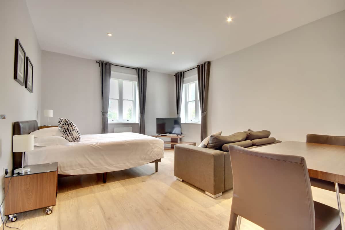 A modern hotel room with a bed, a sofa, a dining table, and a TV.