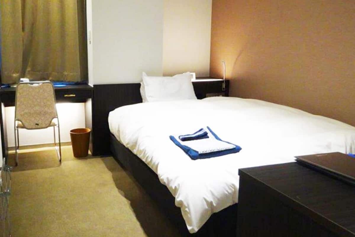 Una habitación de hotel con una cama, un escritorio, una silla y un cesto de basura.