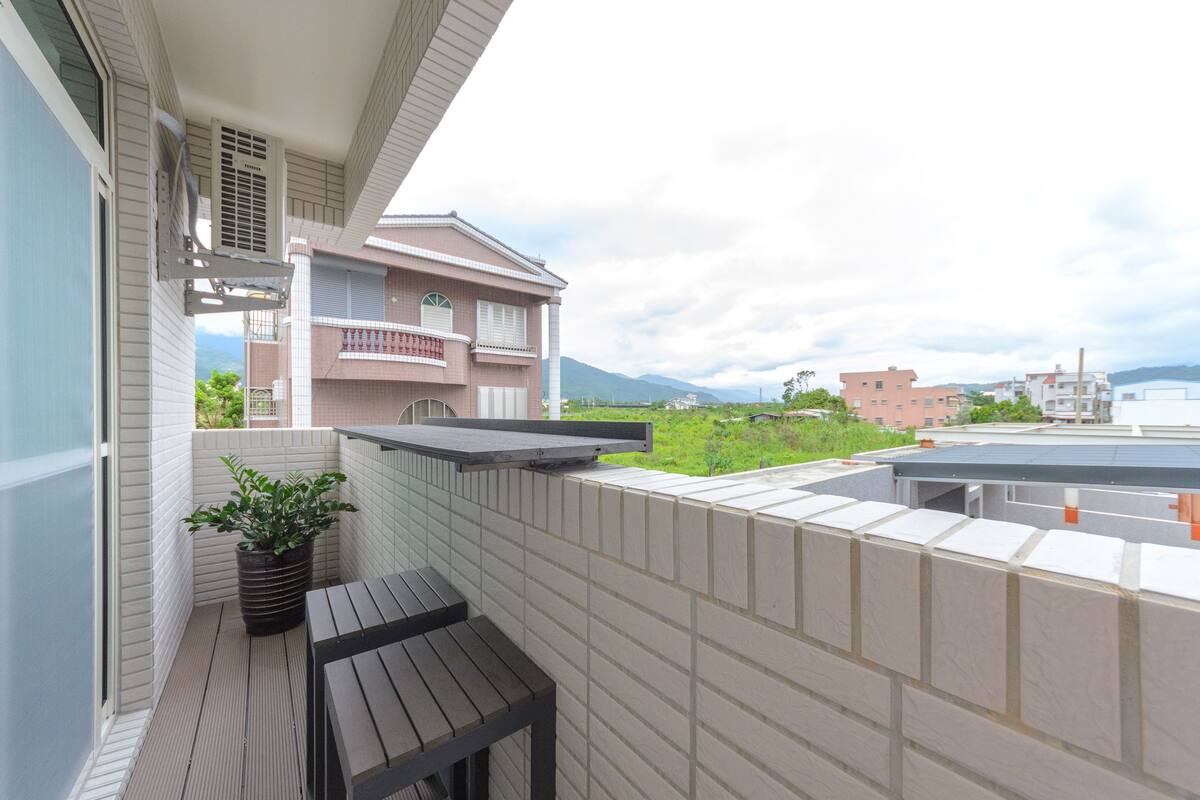 Uma varanda com mesa de madeira, um vaso de planta e vista para um edifício com varanda.