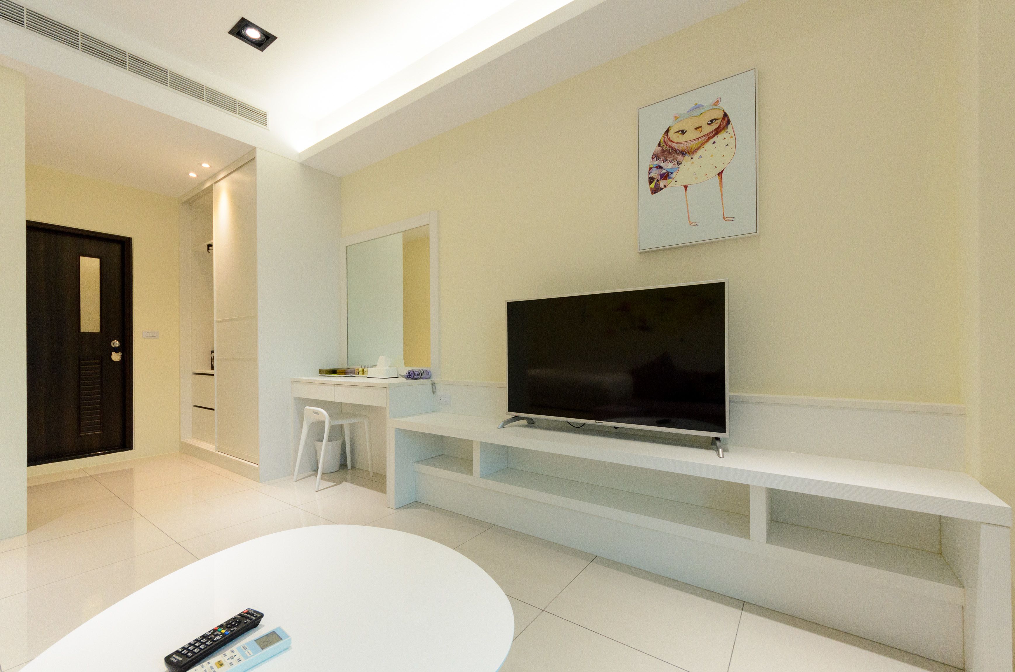A modern living room with a flat-screen TV, white entertainment unit, and a white round table.