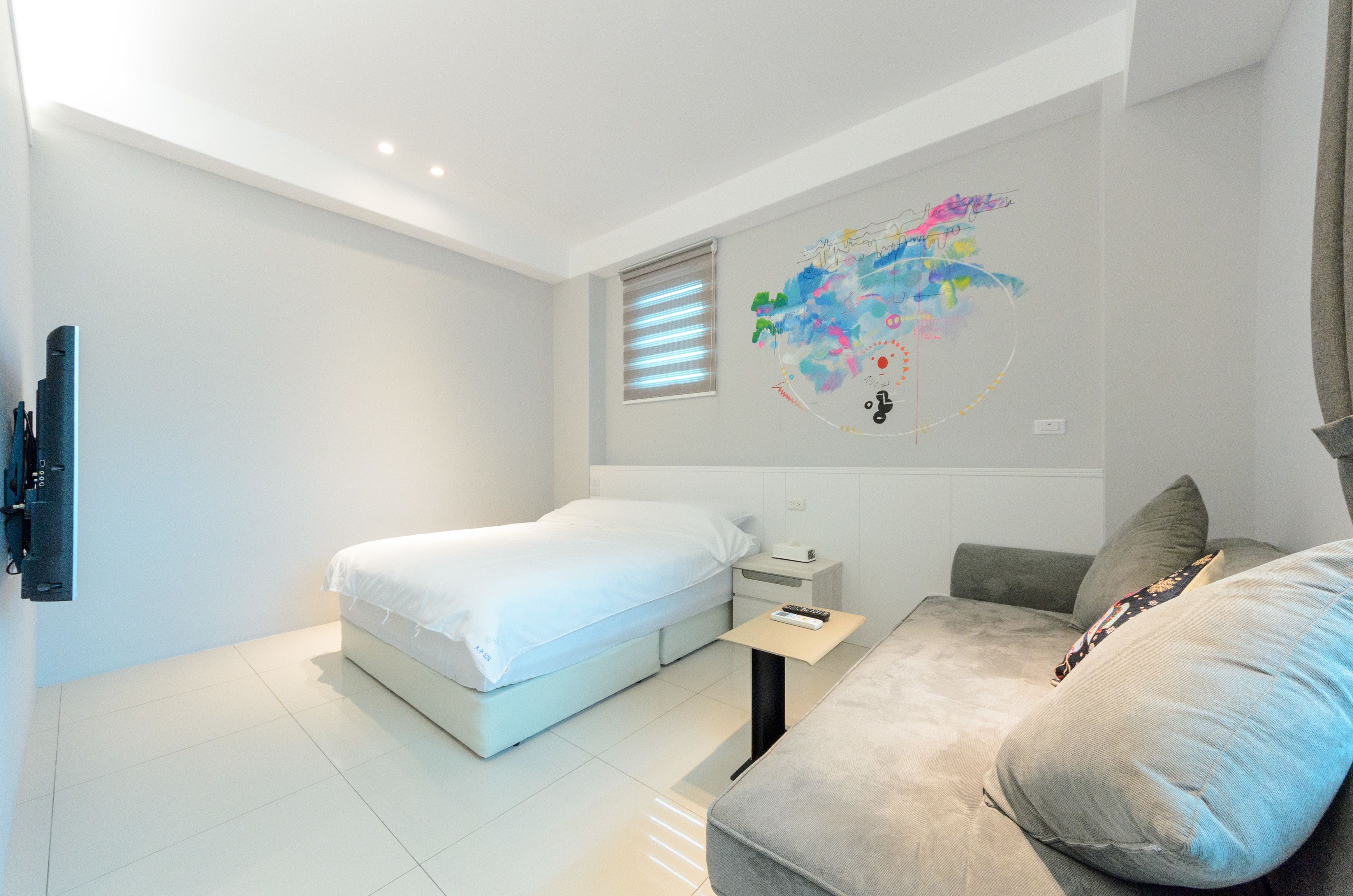 Ein modernes Hotelzimmer mit Bett, Sofa, kleinem Tisch und einem an der Wand befestigten Fernseher.