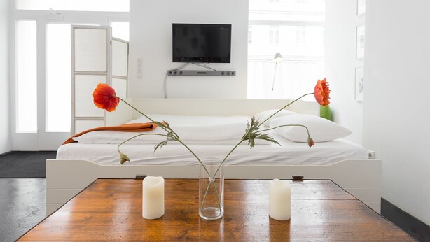Una habitación de hotel moderna con una cama, un televisor montado en la pared y una mesa de madera con velas y flores.
