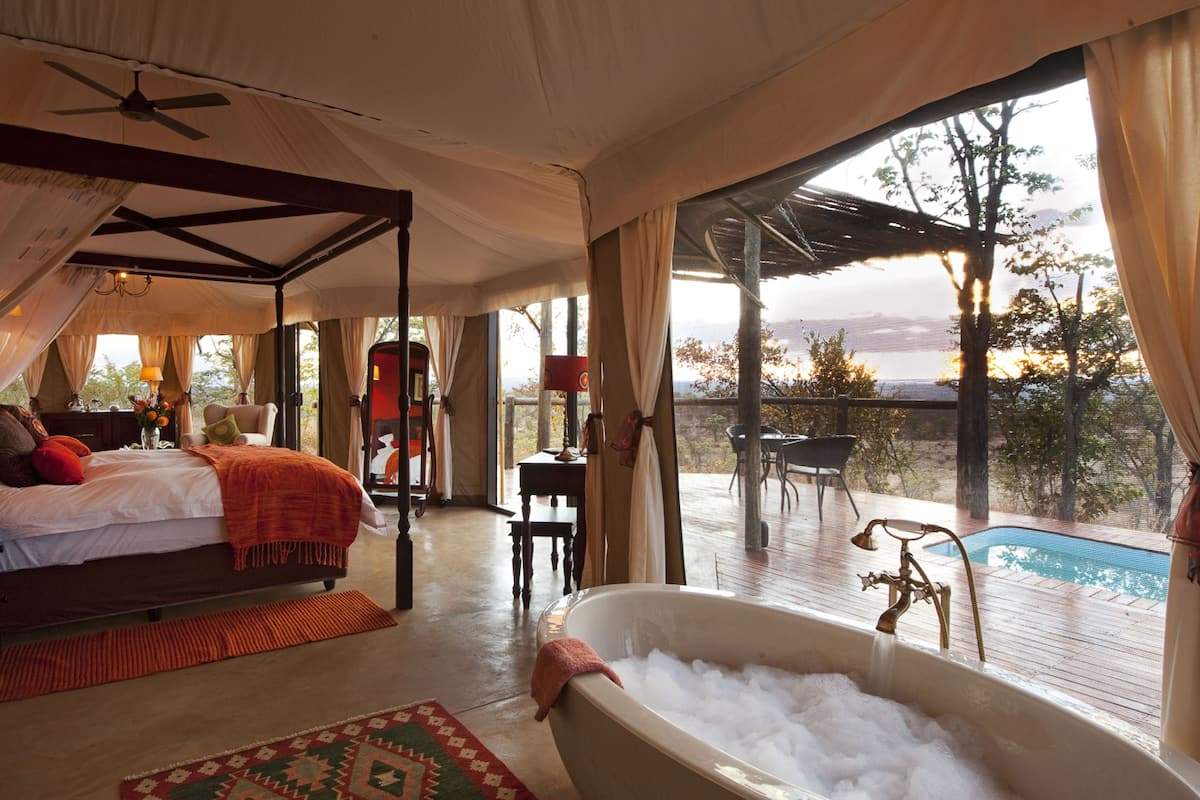 Um quarto espaçoso com uma cama grande, um espaço de estar com mesa e cadeiras, e vista para uma piscina.