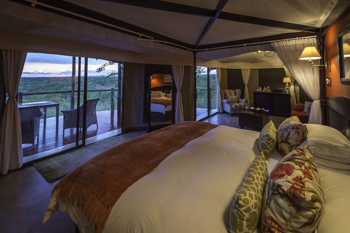 Quarto com uma cama grande, área de estar com mesa e cadeiras, uma escrivaninha pequena e vista para o exterior.