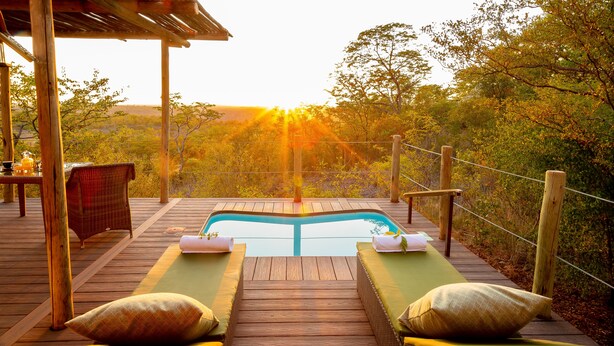 A wooden deck with a pool, lounge chairs, and a table with tea set. - The Elephant Camp (Victoria Falls)