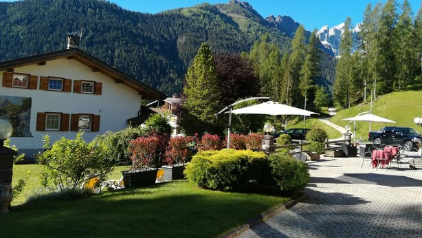 A mountain lodge with a paved driveway, outdoor seating, and a view of the surrounding mountains. - Park Hotel Arnica (Falcade)