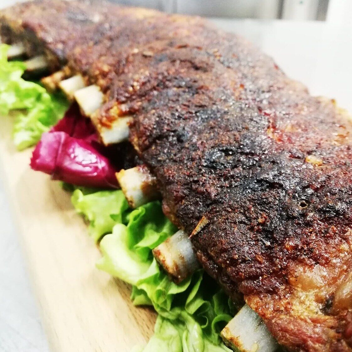 A roasted pork loin with a crispy skin, served on a wooden board with lettuce and red cabbage.