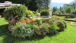 A garden with a fountain, surrounded by various plants and flowers. - Park Hotel Arnica (Falcade)
