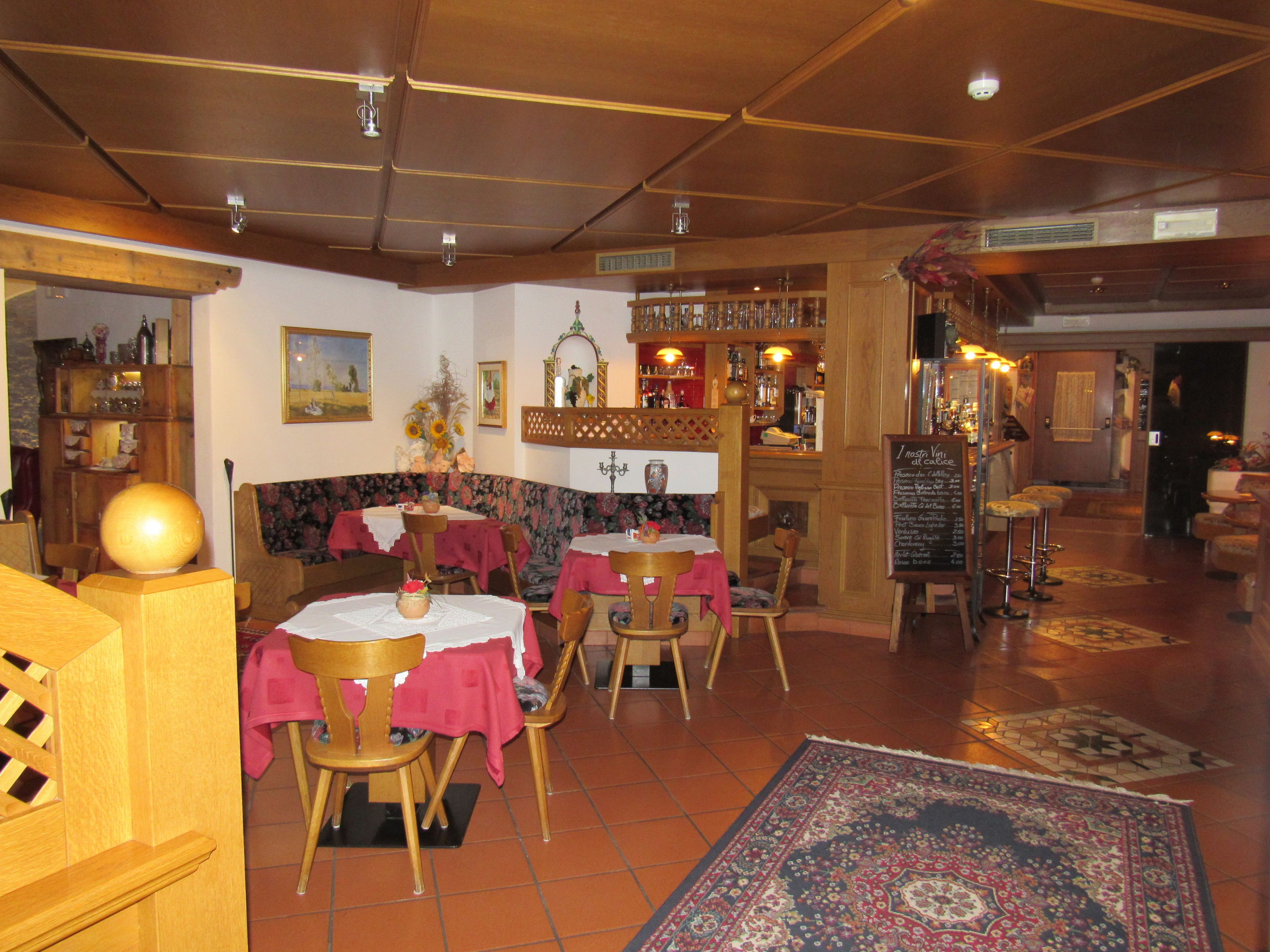A restaurant interior with wooden furniture, red tablecloths, and a patterned rug.
