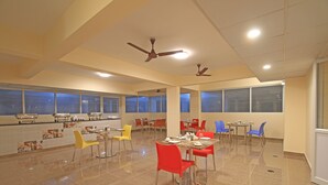 Un comedor amplio con varias mesas y sillas, ventiladores de techo y ventanas grandes.