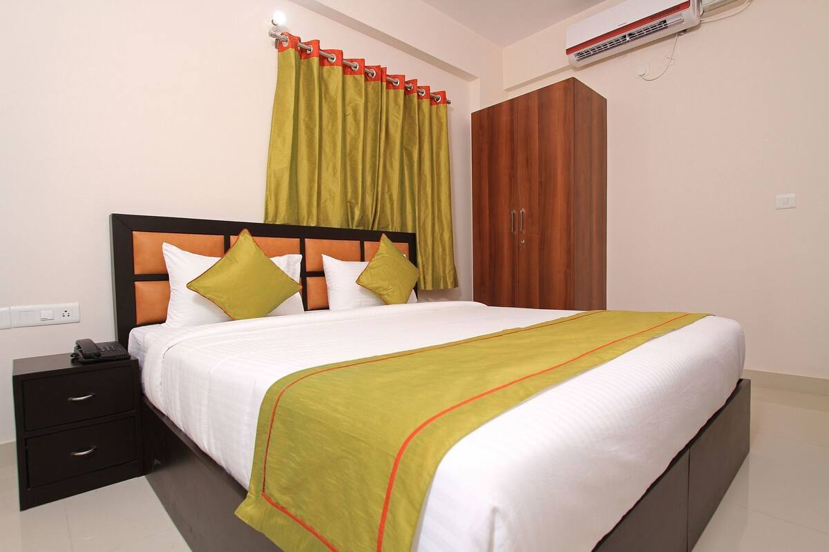 Una habitación de hotel con cama, mesita de noche, armario y equipo de aire acondicionado.