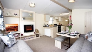 A compact living space with a sofa, a TV, a dining table set, a kitchen area, and a small seating area.