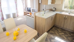 A compact kitchen with wooden cabinets, a dining table with orange juice, and a TV in the background.