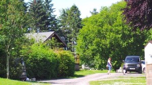 A rural road with a house on the left, a person walking, and a parked car on the right.