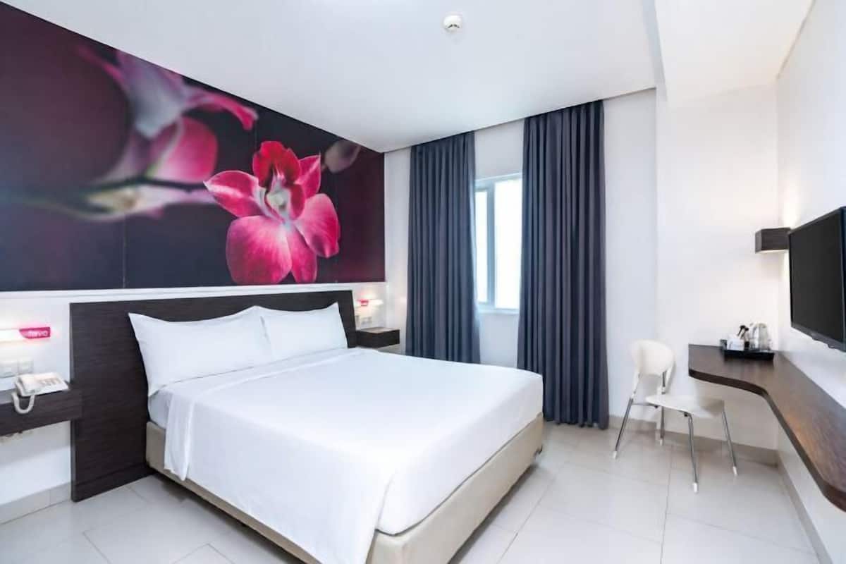 A modern hotel room with a large bed, a desk, a chair, a flat-screen TV, and a wall-mounted phone.