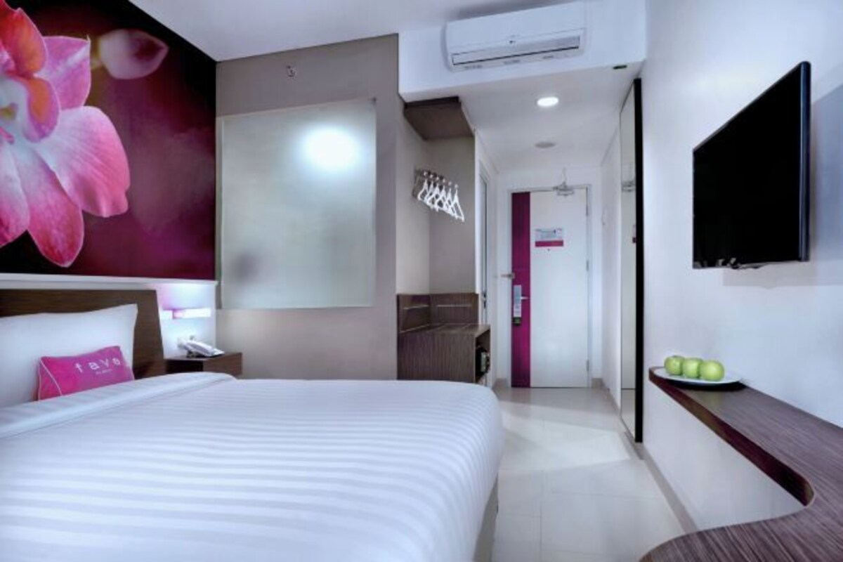 A modern hotel room with a large bed, a flat-screen TV, a vanity with a mirror, and a wall-mounted air conditioner.