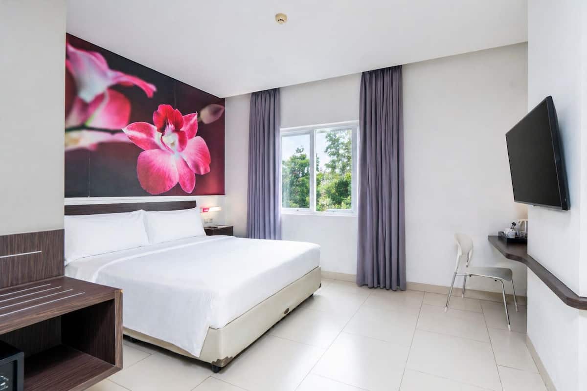 A hotel room with a large bed, a desk, a chair, a TV, and a window with curtains.