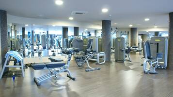 Un gimnasio con diversas máquinas de ejercicio, espejos y suelo de madera.