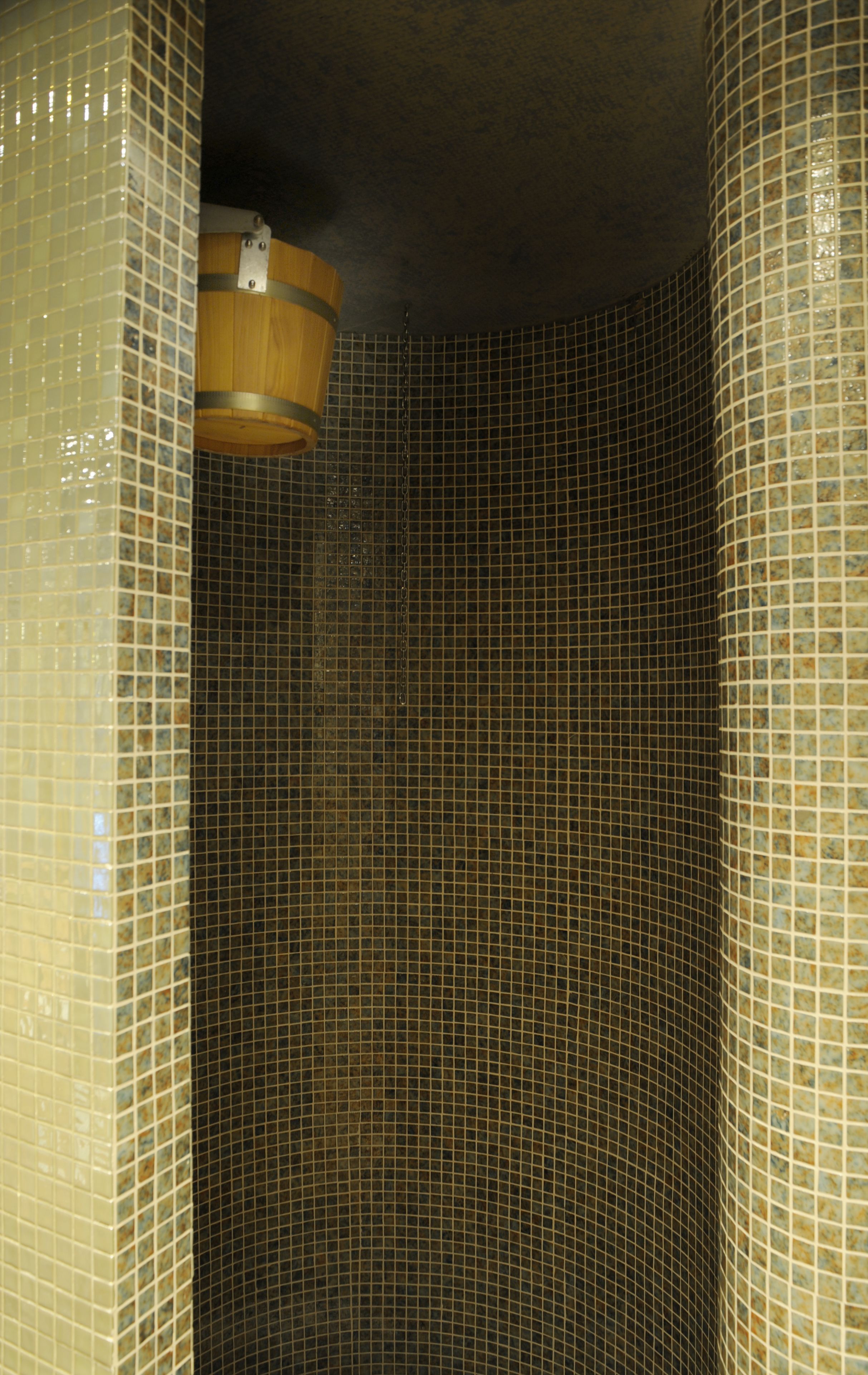 A tiled shower with a wooden bucket hanging from the ceiling.