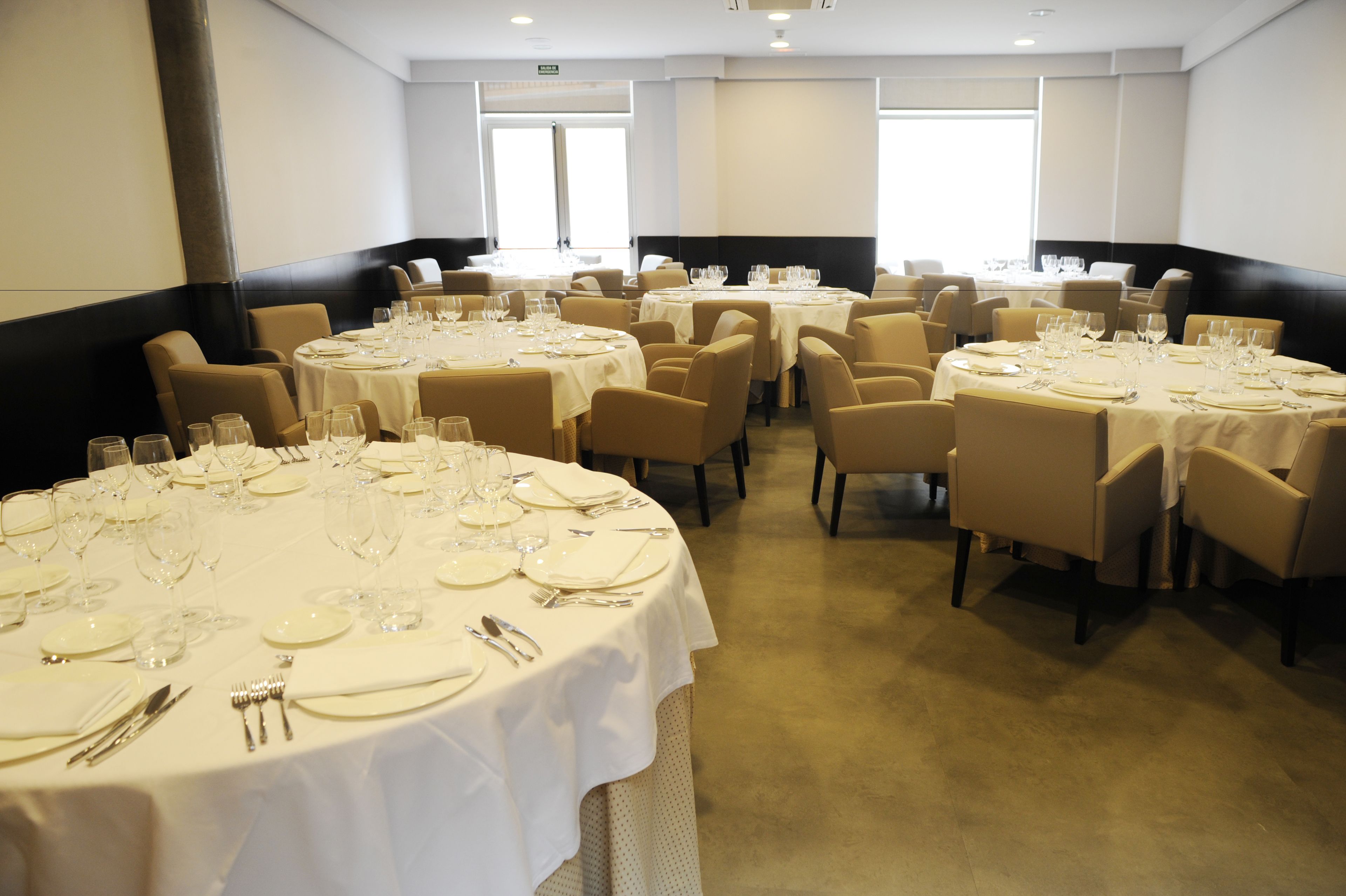 Une salle à manger d’hôtel avec plusieurs tables rondes dressées pour le repas, chacune étant recouverte d’une nappe blanche et agrémentée de couverts en argent.