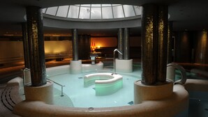 A modern indoor pool with a circular design, surrounded by tall pillars, and a skylight above. - Cumbria Spa & Hotel (Ciudad Real)