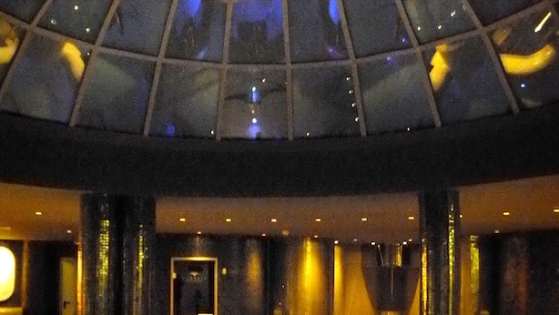 A large indoor swimming pool with a central circular feature, surrounded by a tiled floor and a glass ceiling. - Cumbria Spa & Hotel (Ciudad Real)