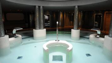 A modern indoor pool with a central fountain, surrounded by seating areas and a high ceiling.