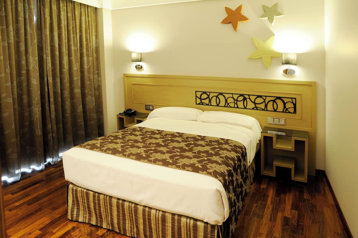 A neatly made bed with a patterned bedspread, two bedside lamps, and a nightstand with a phone.