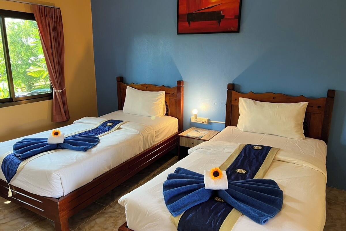 Dos camas dobles con toallas y almohadas azules a juego, un cuadro en la pared y una ventana con cortinas.