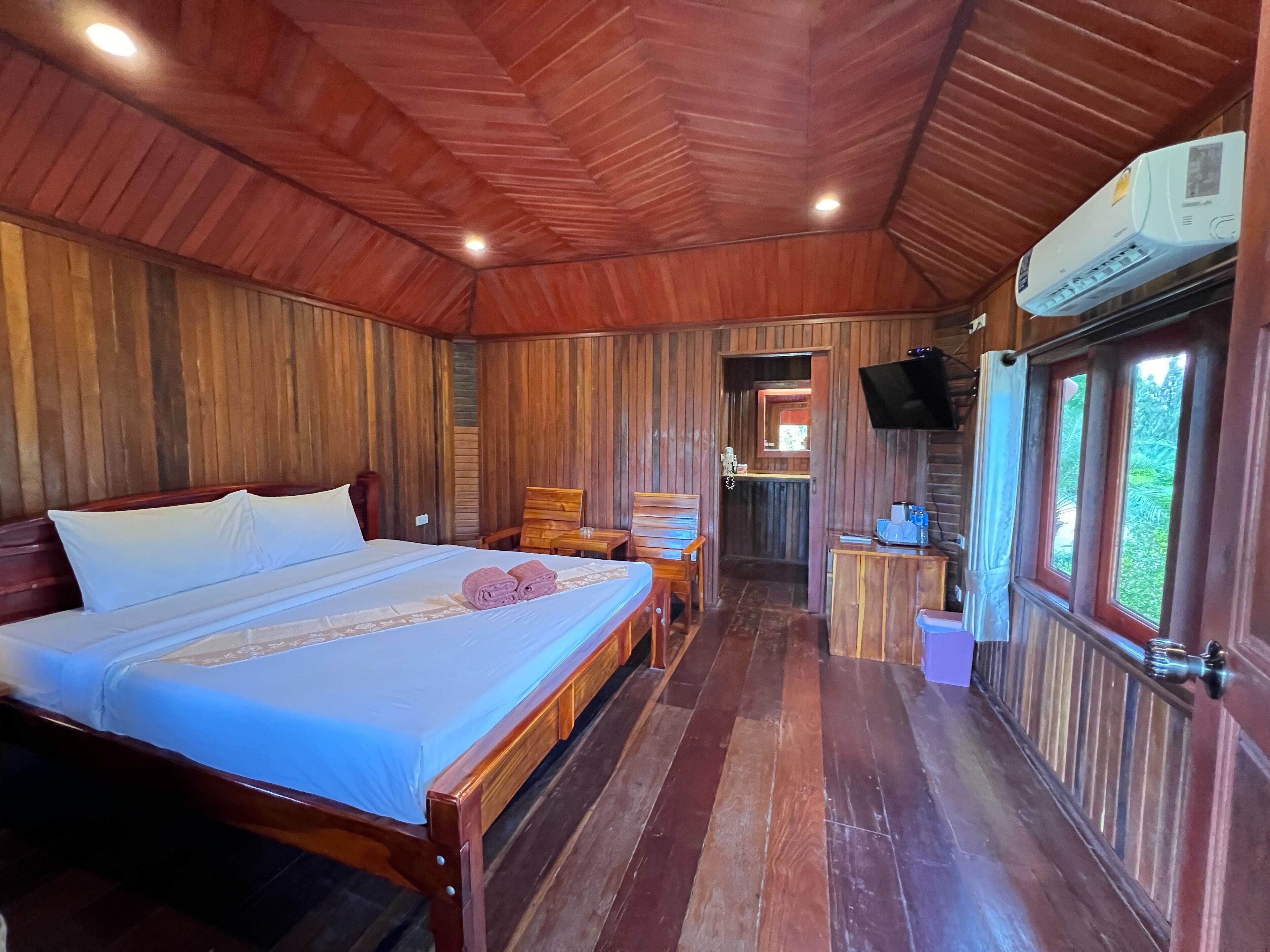 Una habitación de madera con una cama, un televisor y una ventana.