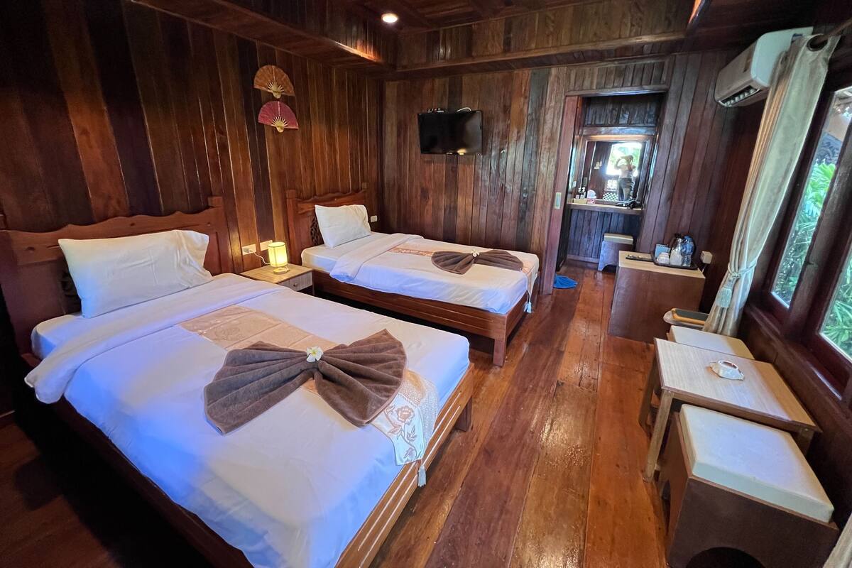 Una habitación de madera con dos camas, una mesita y un televisor fijado a la pared.