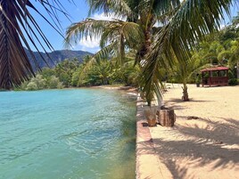 Uma praia com águas turquesa cristalinas, palmeiras e uma estrutura de madeira.
