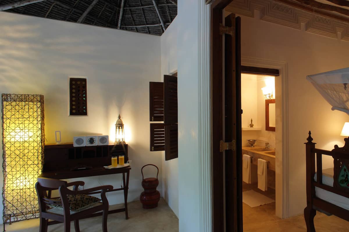 A bedroom with a canopy bed, a desk with a lamp, and a view of the outside.