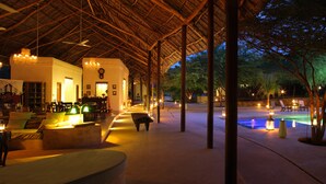 Un'area esterna ben illuminata con piscina, lettini e una zona salotto coperta.