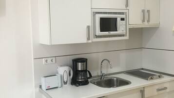 A modern kitchen with white cabinets, a built-in microwave, a coffee maker, and a sink.