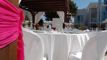 An outdoor dining area with white tablecloths and chairs, set up under a wooden pergola.