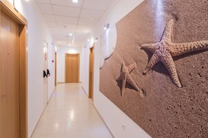 Un pasillo de hotel con puertas de madera, piso de baldosas y un mural en la pared con estrellas de mar.