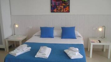 A hotel room with a bed, blue pillows, white headboard, two bedside tables with lamps, and a colorful artwork on the wall.