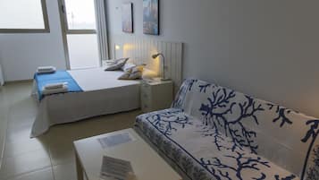Una habitación de hotel con cama, sofá, mesita de noche y ventana.
