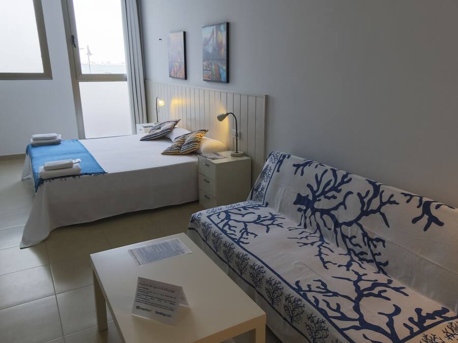 Una habitación de hotel con cama, sofá, mesita de noche y ventana.
