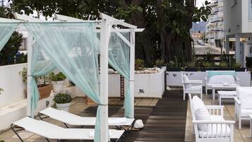 A rooftop terrace with white lounge chairs, a canopy structure, and potted plants.
