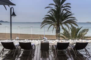 A deck with four lounge chairs, a small table, and a bottle of champagne. The deck overlooks a beach with white pebbles and palm trees. - El Secreto del Agua (Cartagena)