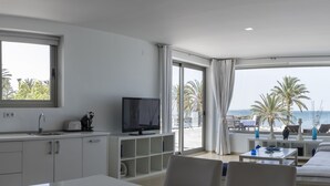 A modern hotel room with a kitchen, a TV, a sofa, and a balcony with a view of the sea and palm trees. - El Secreto del Agua (Cartagena)