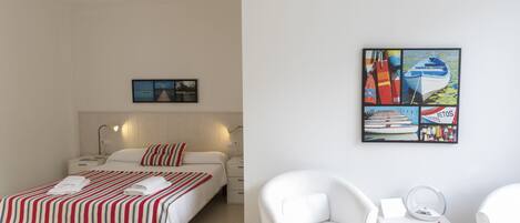 Une chambre à coucher comprenant un lit, des tables de chevet, une commode, une chaise, une petite table avec un miroir et une œuvre d’art murale.