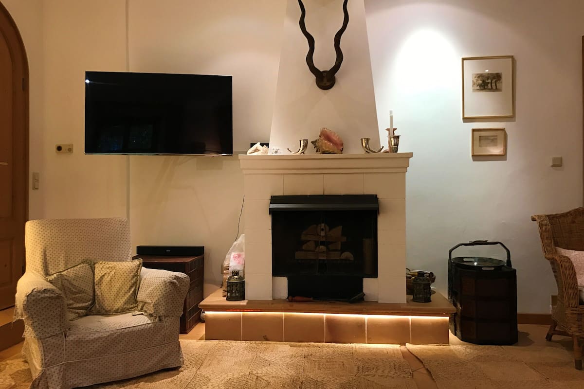 A living room with a fireplace, a television mounted on the wall, and a comfortable seating area with a patterned sofa and a wicker chair.
