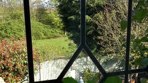 Vista a través de una ventana con un diseño geométrico, mostrando un jardín con césped, una valla de madera y diversas plantas.