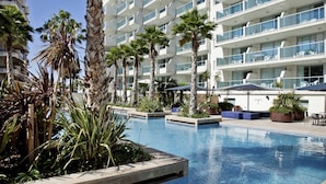 Un hotel moderno con zona de piscina, palmeras y mobiliario exterior.