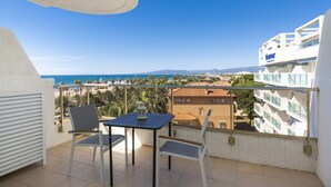 Un balcón con mesa y sillas, con vista a una playa y edificios.